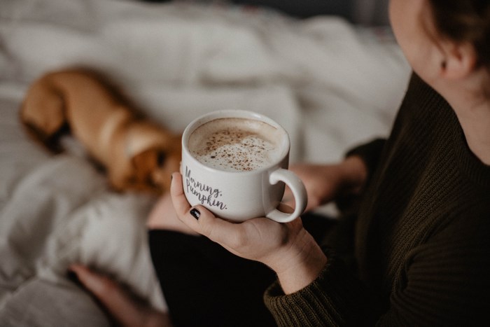 Woman holding a coffee mug with a dog in the background