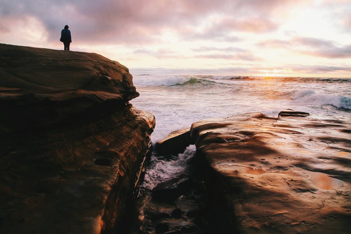 Person standing on a rock overlooking the ocean at sunset