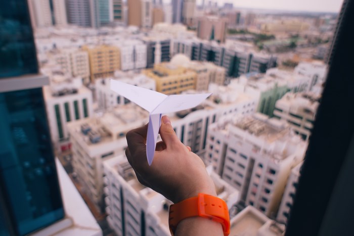 Hand holding a paper airplane over a city in UAE