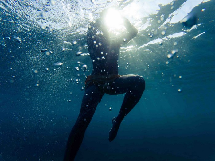 Person swimming underwater with sun rays and bubbles
