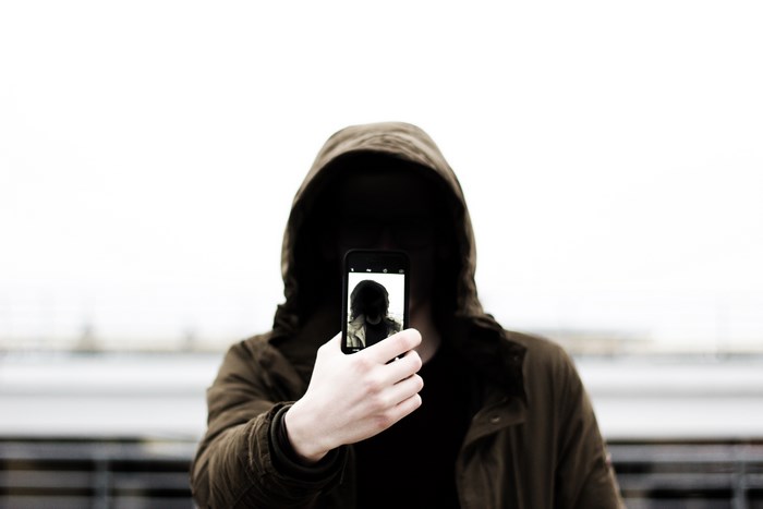 Person in a hoodie taking a selfie with an iPhone