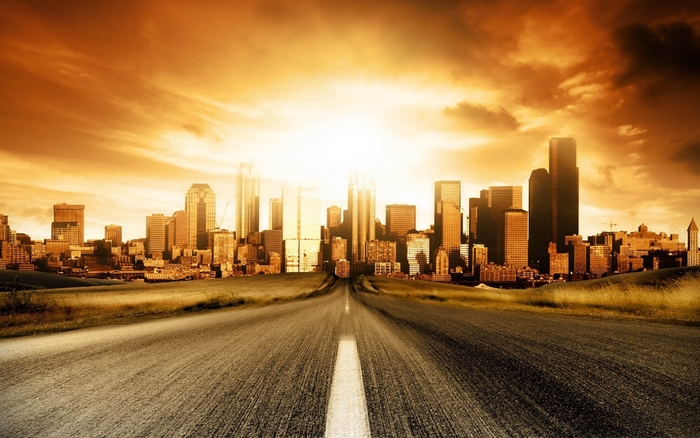 Road leading to a modern city skyline at sunset