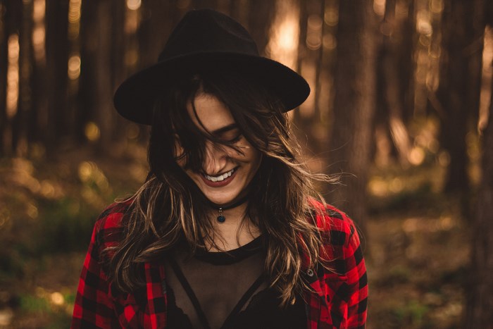 Woman in a hat and plaid shirt smiling in a forest