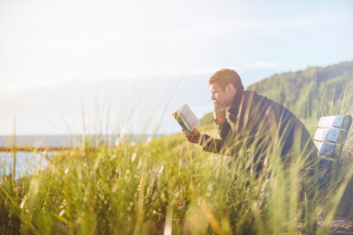 Man reading a book on a bench by the water