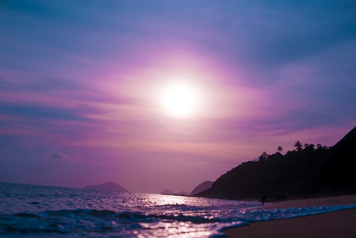 Purple sunset over a tropical beach with ocean waves