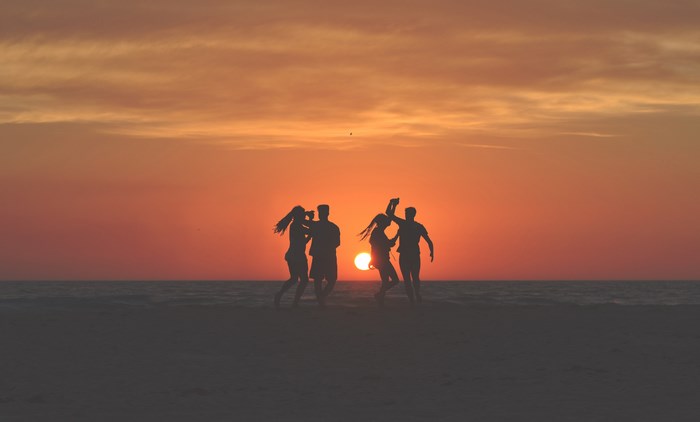 Four friends dancing on the beach at sunset