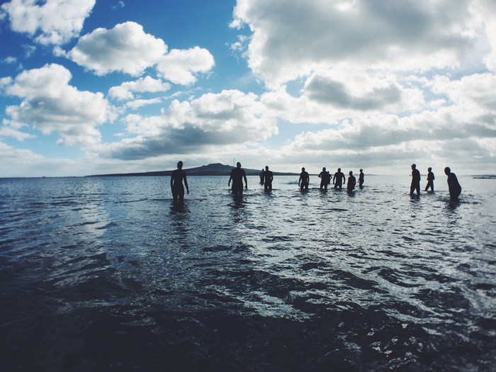 Group of people wading in the ocean towards a volcano island