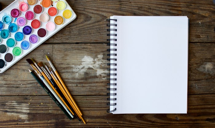 Watercolor paint palette, brushes, and notebook on wood