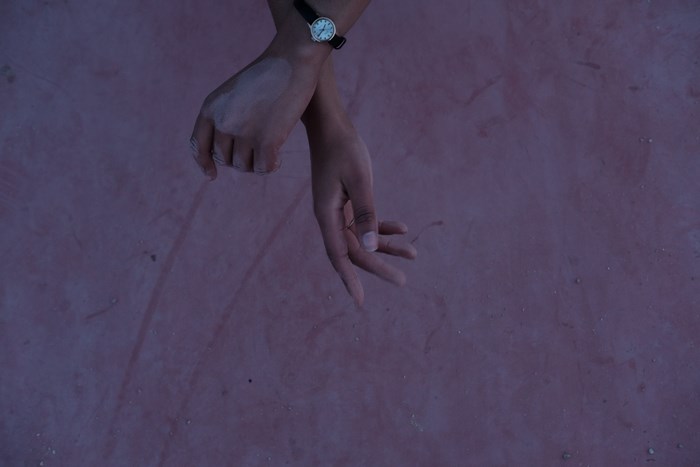 Hands with a watch crossed over a pink surface