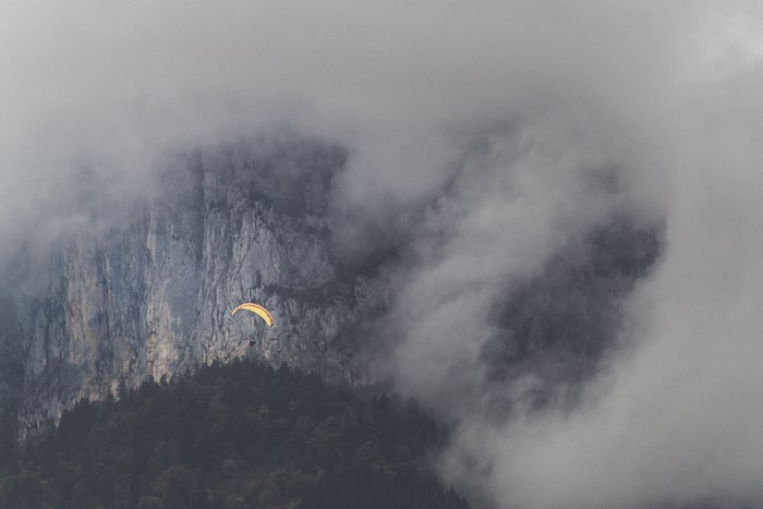 Paraglider flying near a foggy mountain cliff