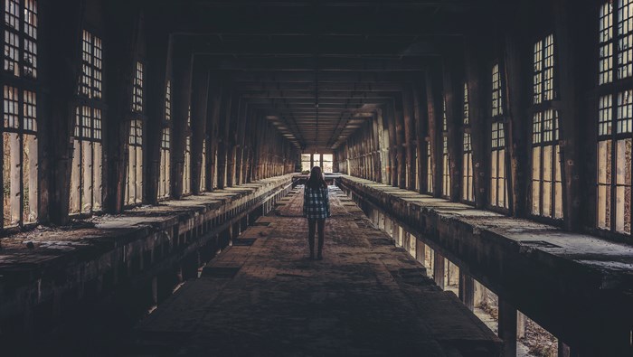 Woman standing in a long, abandoned corridor with windows