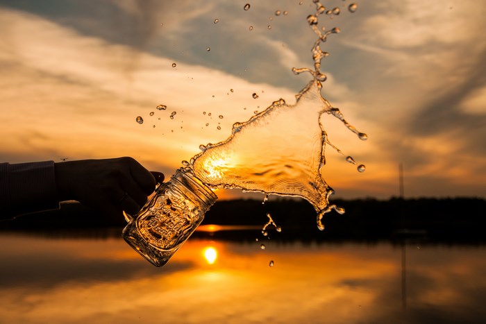 Hand tossing a mason jar with water splash at sunset