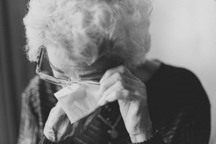 Elderly woman with glasses crying and wiping her eyes