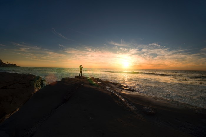 Man standing on rocks at sunset overlooking the ocean