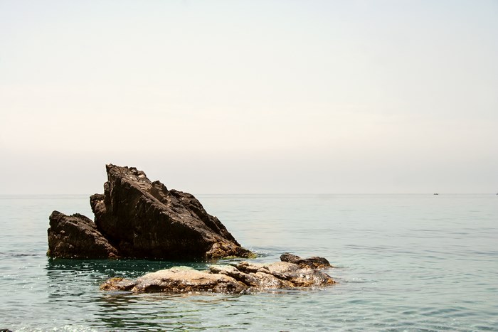 Rocky outcrop in the open sea under a hazy sky