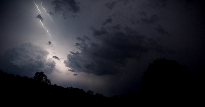 Lightning strike over dark clouds and trees at night