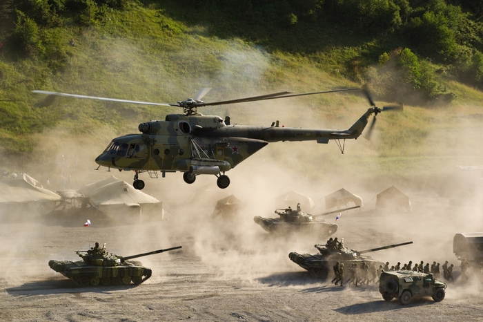 Military helicopter and tanks in a dusty field
