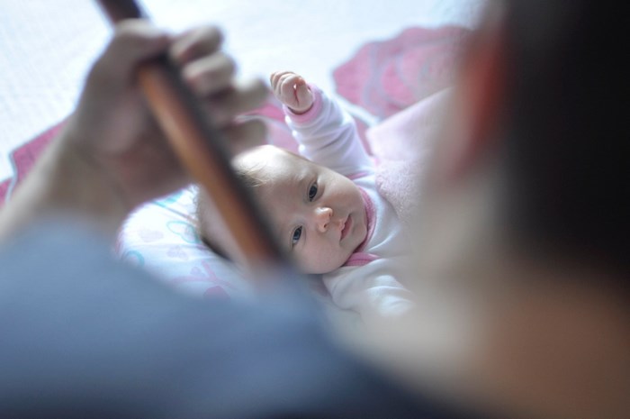Baby lying down with a hand holding a wooden object