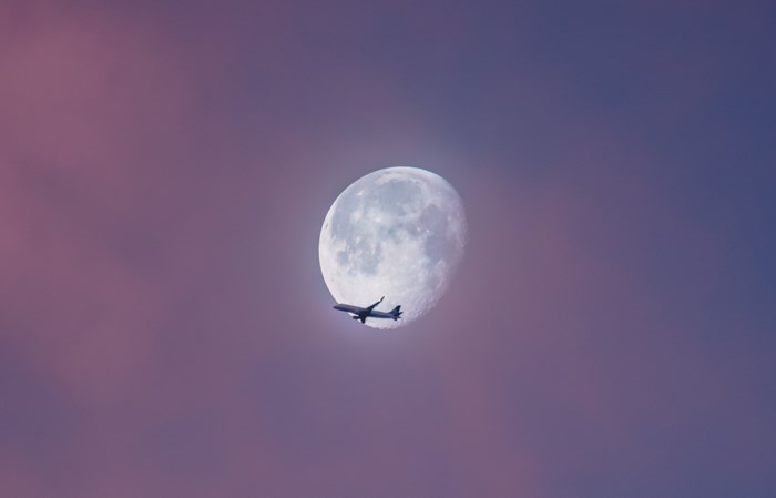 Airplane flying past the moon in a pink and purple sky