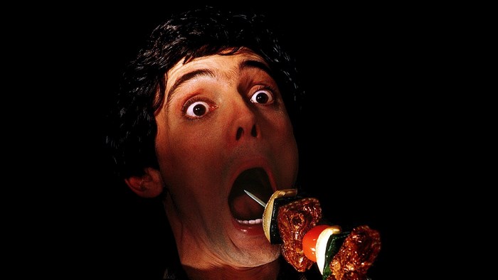 Man eating a skewer of meat and vegetables