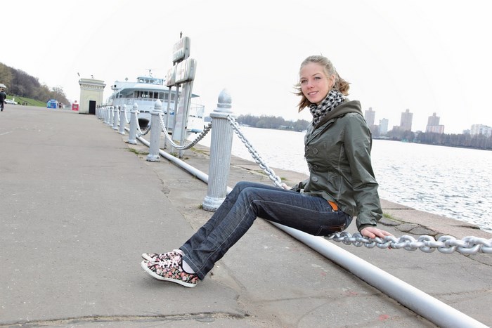 Young Woman Sitting on Chain Fence by Waterfront
