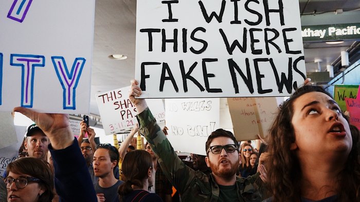 Protesters hold signs including "I WISH THIS WERE FAKE NEWS"