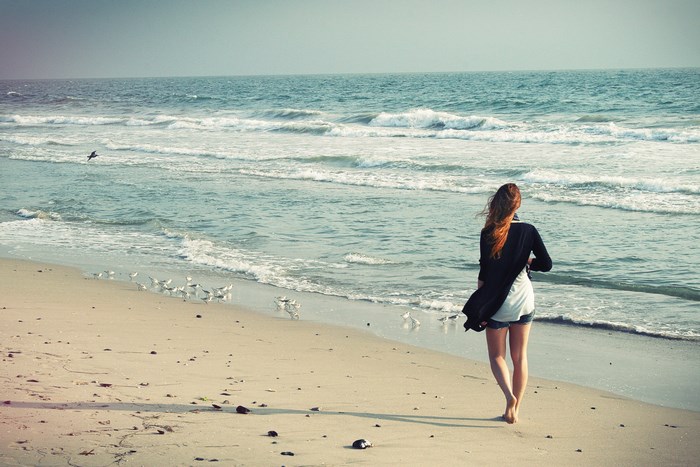 Woman walking on a beach with birds and the sea