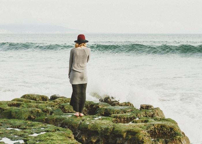 Woman in red hat on mossy rocks by the ocean