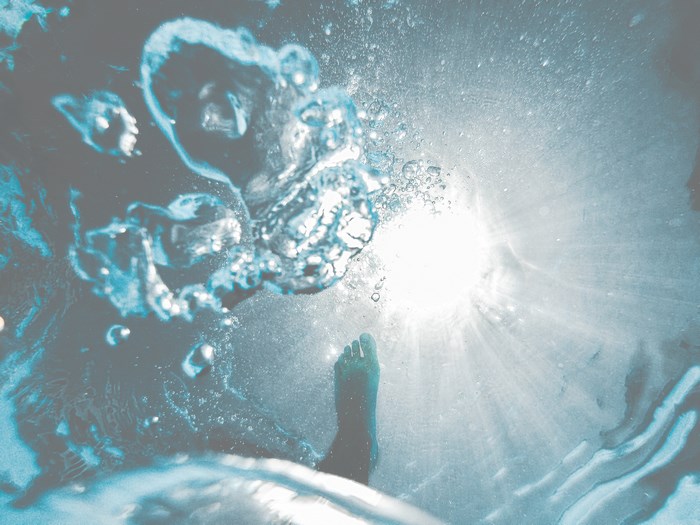 Underwater view of a person's foot with sun rays
