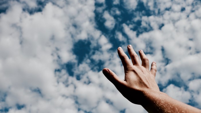 Hand reaching up towards the sky and clouds
