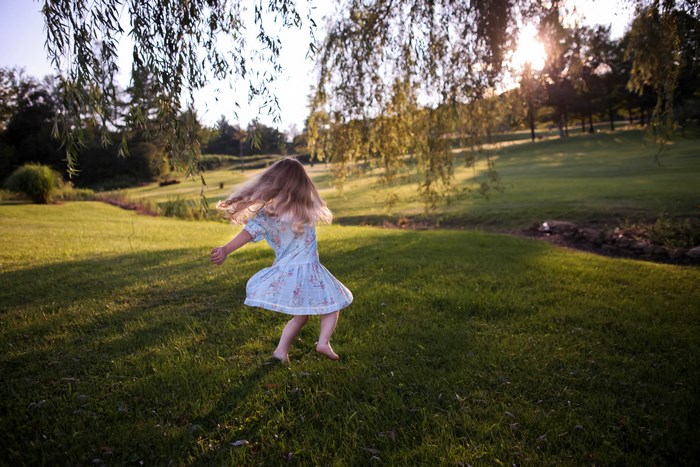 Girl in a dress spinning in a grassy meadow