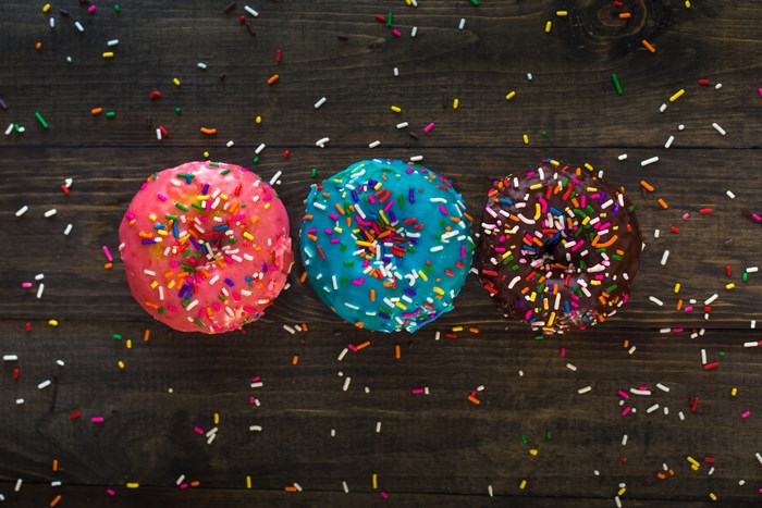 Colorful Frosted Donuts with Sprinkles on Wooden Table