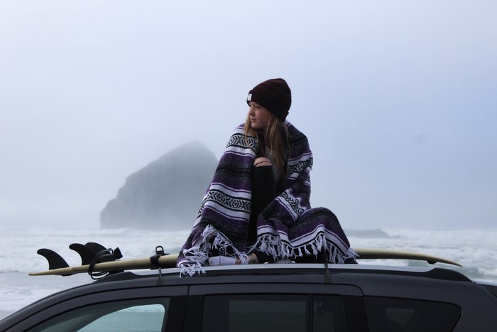 Woman wrapped in blanket on car roof with surfboard