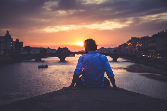 Man sitting on bridge watching sunset over river