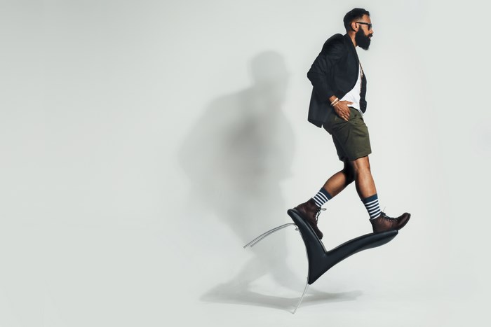 Man in blazer and shorts walking on a chair