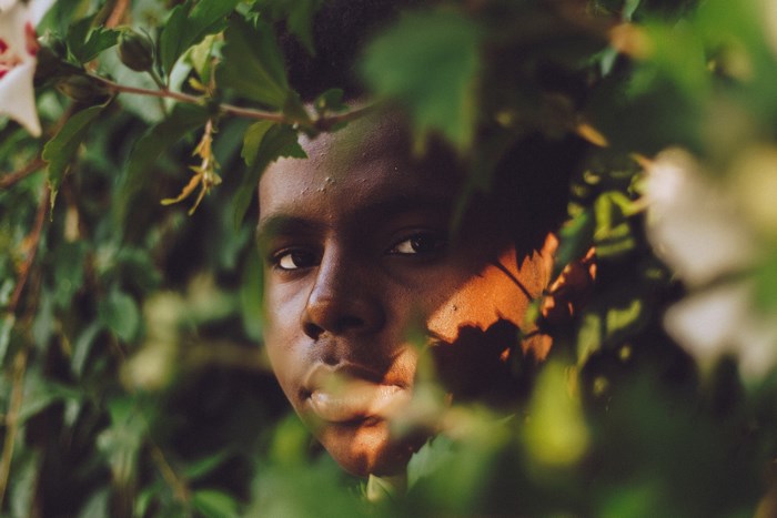 Young Black Man Peeking Through Green Foliage