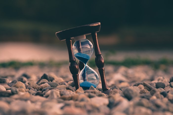 Hourglass with blue sand on a rocky ground