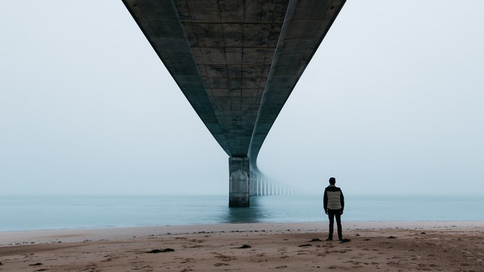 Man standing on beach under a large concrete bridge