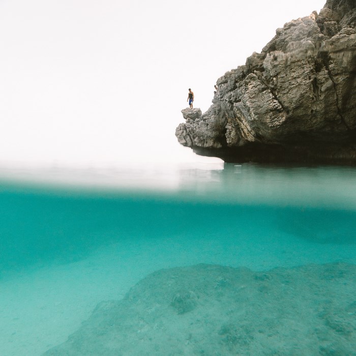 Person standing on a rock cliff above turquoise water