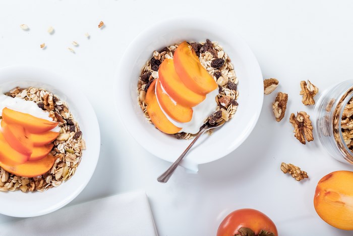 Two bowls of granola with persimmon slices and yogurt