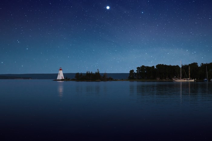 Lighthouse on an island at night under a starry sky