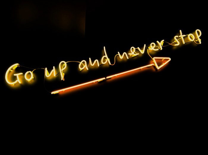 Neon sign 'Go up and never stop' with arrow