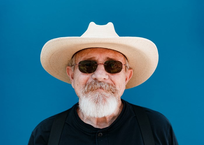 Old man with beard and hat against blue background