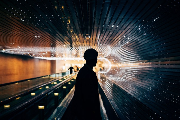 Silhouette of a man on an escalator in a tunnel with lights