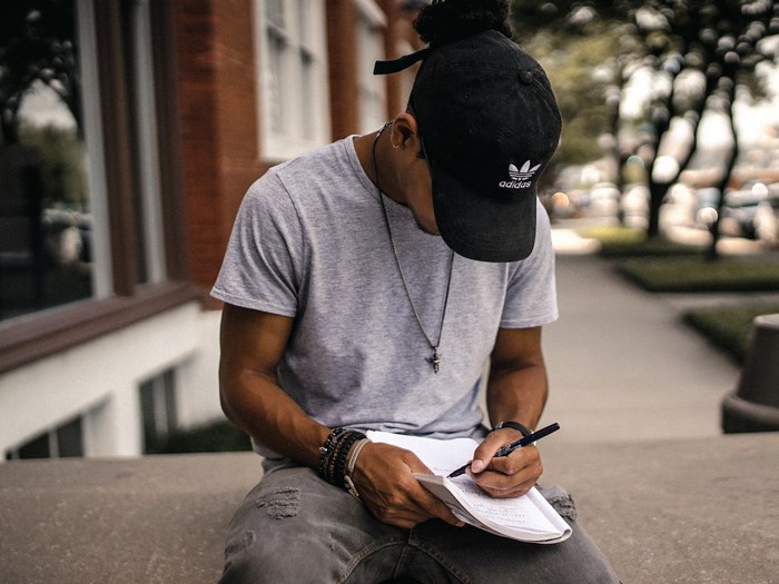Man wearing Adidas cap writing in a notebook