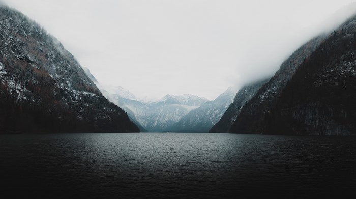 Dark Lake Between Snowy Mountains in Fog