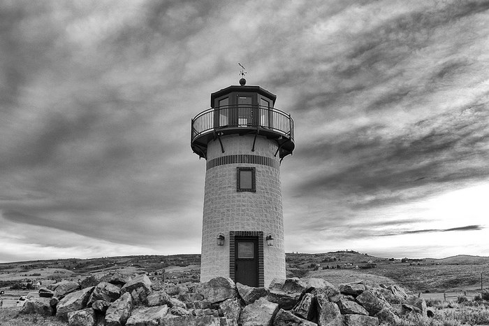 Black and white lighthouse on a rocky hill under a cloudy sky
