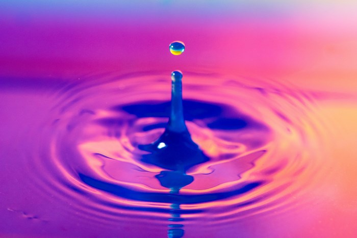 Water droplet splashing into purple and pink water