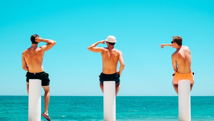 Three men sitting on poles by the Mediterranean Sea