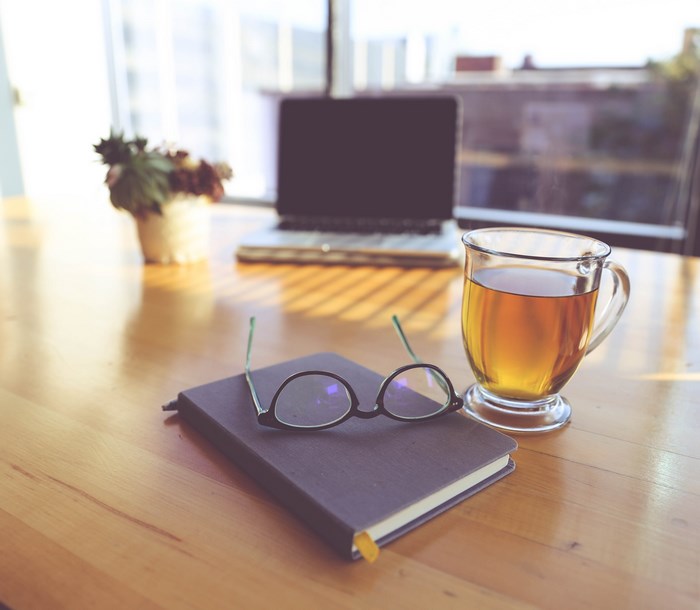 Desk with laptop, tea, notebook, and glasses